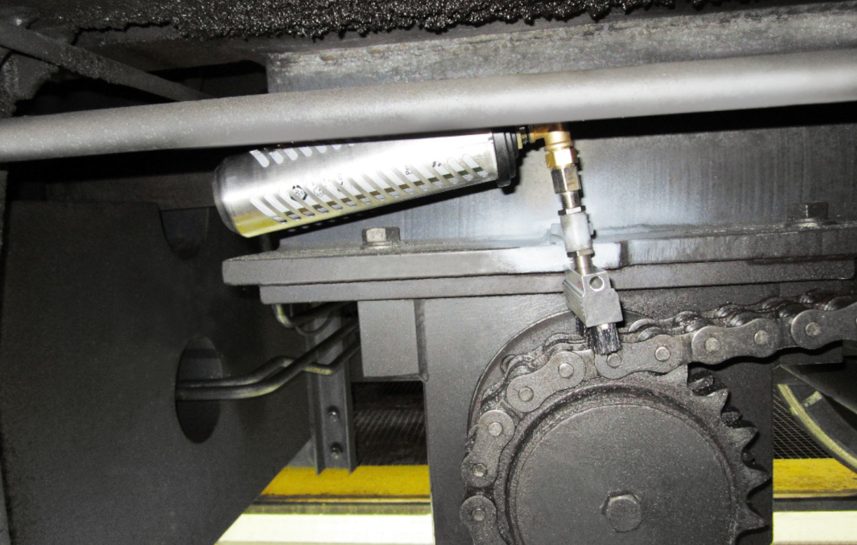 Der simalube 250ml Schmierstoffspender schmiert die Antriebskette eines Schienenbaukrans. Der Spender wird dabei zusätzlich von einer Schutzhaube geschützt.